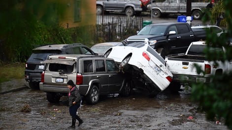A woman walks by cars damaged by floods during a rainstorm in San Diego on Monday, Jan. 22, 2024. (AP Photo/Denis Poroy)