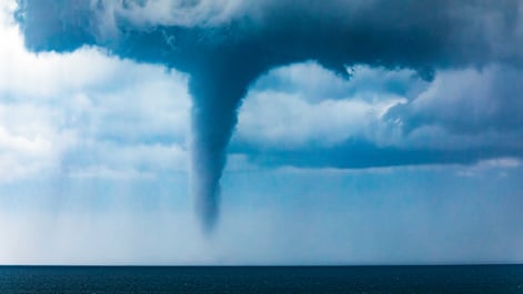 Tornado waterspout in the ocean off the coast with dark dramatic sky, clouds and windy ocean